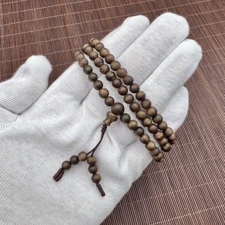 108-bead agarwood mala with guru bead and tassel held on a white glove