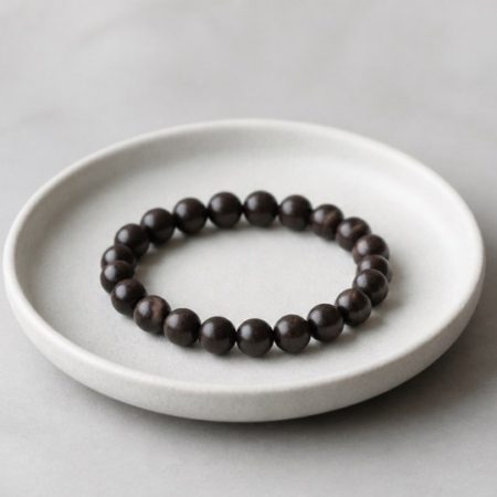 Single unlabelled dark wooden bead bracelet in a plain ceramic dish