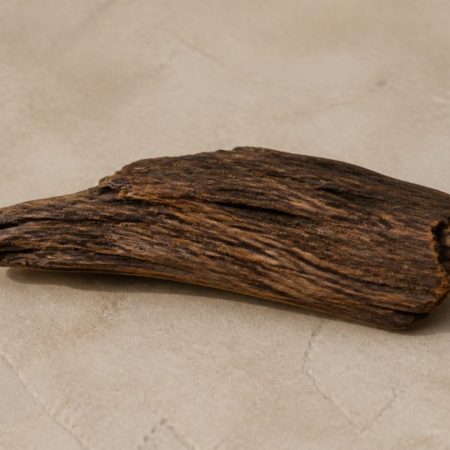 Single unlabelled dark natural wood piece on a plain warm stone surface