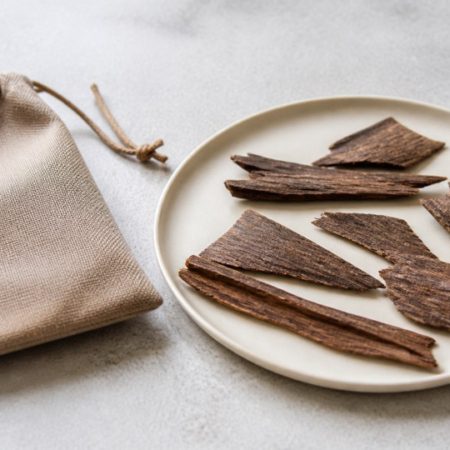 Thin natural wood pieces on a plain ceramic plate beside an unlabelled drawstring pouch