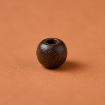 Single unlabelled rounded dark wooden bead on a warm clay-colored surface