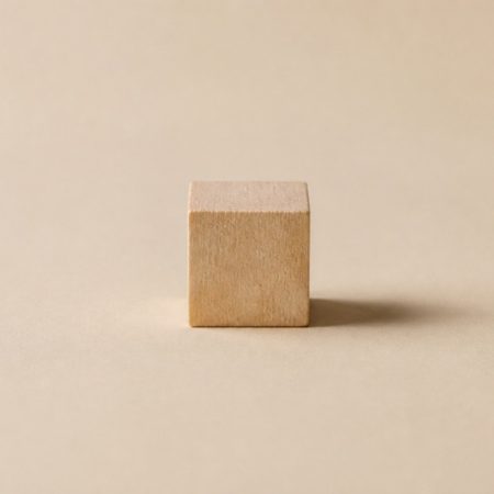 Single unlabelled natural wood cube on a matte sand-colored surface
