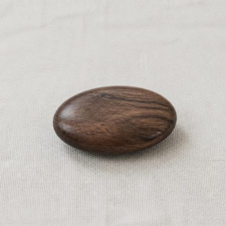 Single unlabelled dark natural wood oval on pale warm-gray fabric